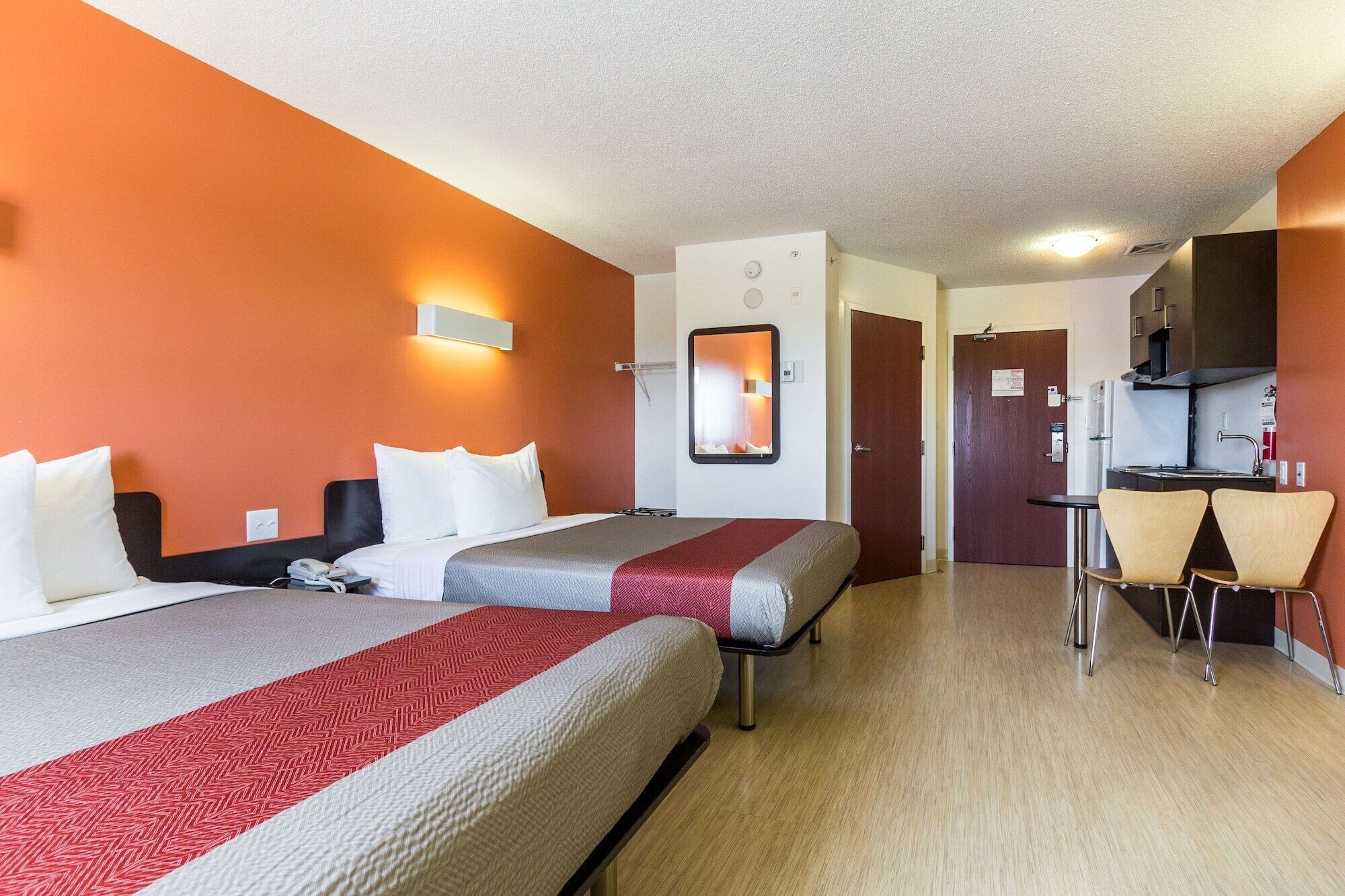 Een hotelkamer met twee bedden, een kleine keukenhoek en een spiegel.