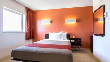 A hotel room with a bed, a nightstand, a wall-mounted mirror, and a window with curtains.