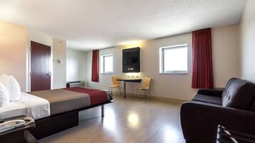 Quarto de hotel com cama, escrivaninha, duas cadeiras, televisão e sofá.