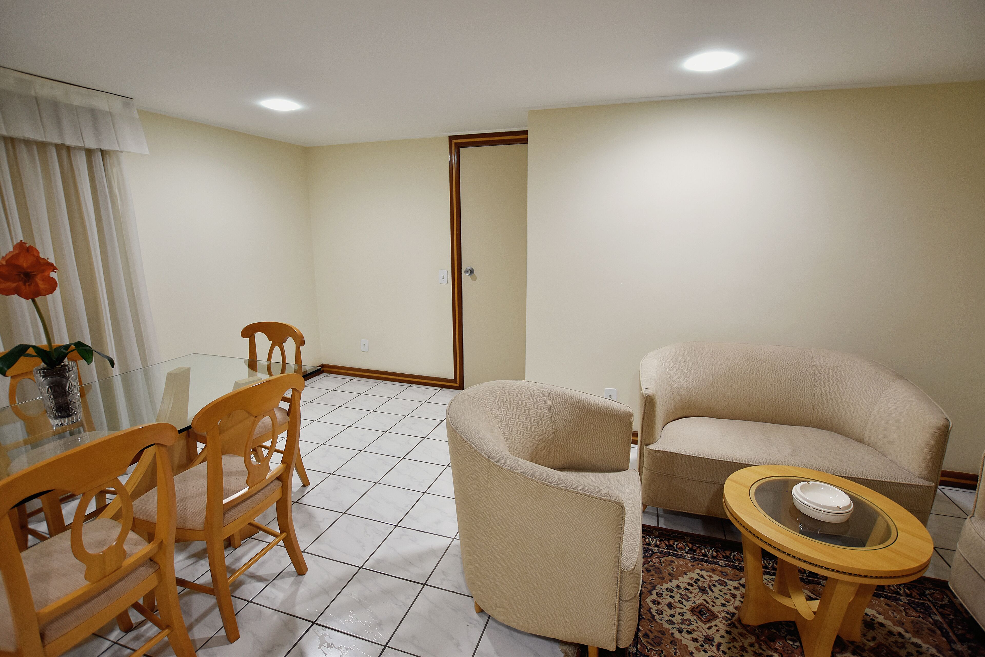 Ein Wohnzimmer mit einem beigefarbenen Sofa, Holzstühlen, einem Glastisch und einem gemusterten Teppich.