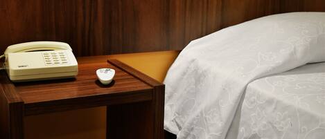 A hotel room with a wooden headboard, a bedside table with a telephone and a remote control, and a bed with a white bedspread.