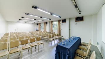A conference room with rows of chairs, a long table with a blue tablecloth, and ceiling lights.