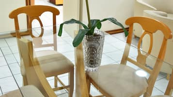 Uma sala de jantar com mesa de vidro, cadeiras de madeira e um vaso com uma única flor.