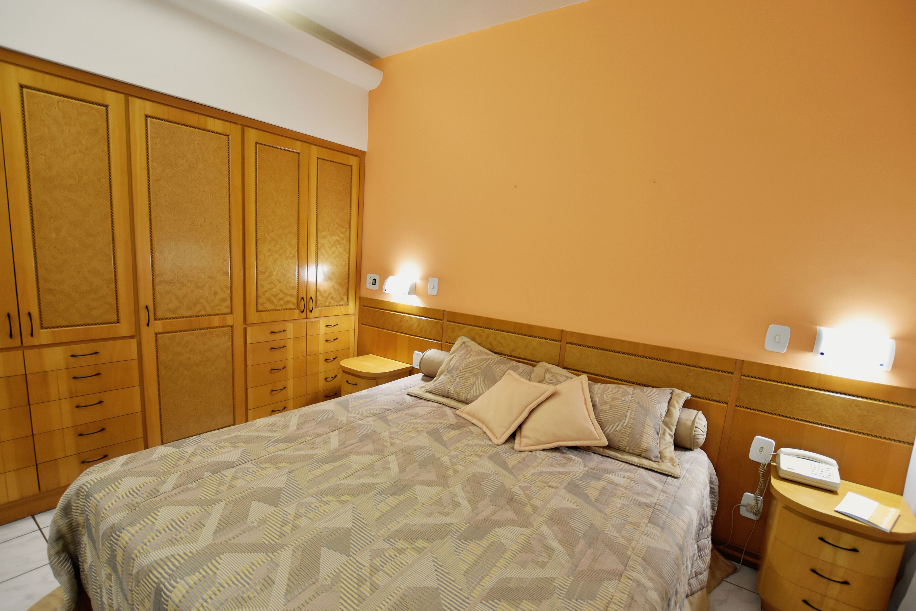 A bedroom with a bed, wooden wardrobe, bedside tables, and a nightstand with a phone.