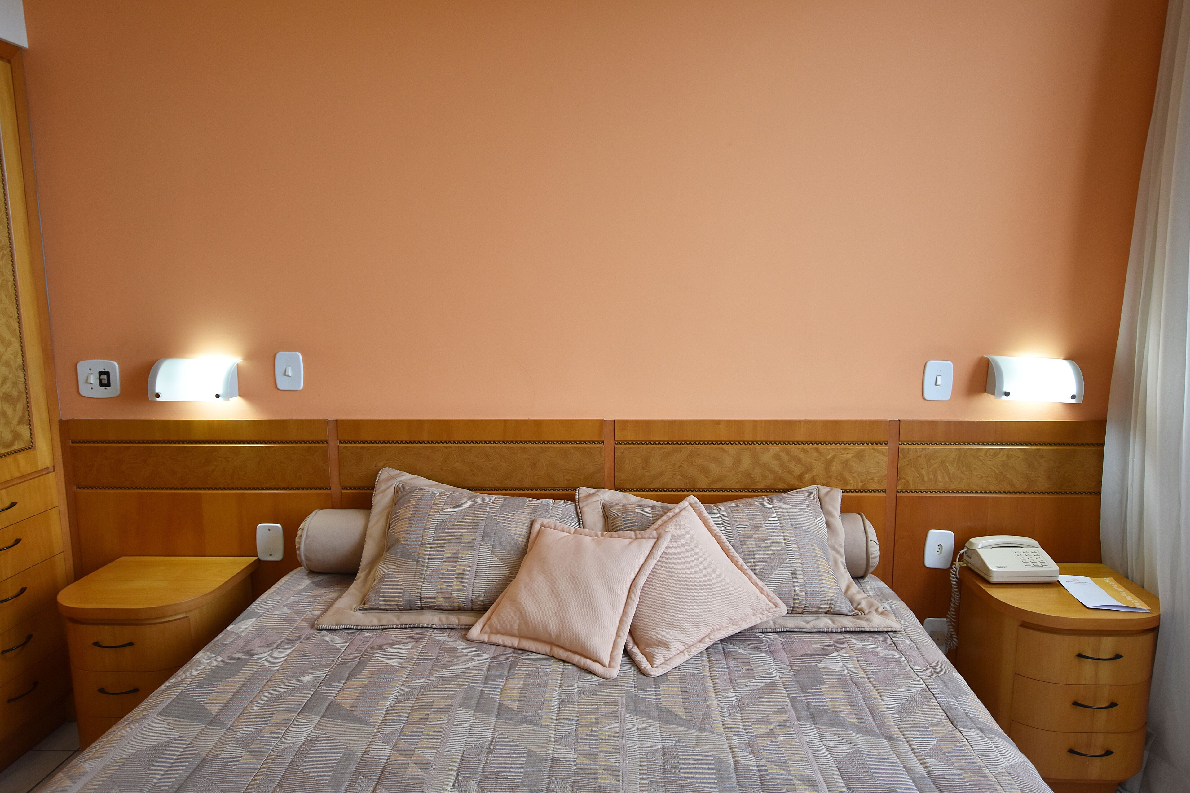 A neatly made bed with a patterned bedspread and two pillows, flanked by bedside tables with lamps and a telephone.