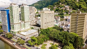 A high-rise building with multiple floors, surrounded by greenery and a river.
