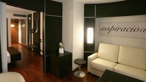 A modern hotel room with a sofa, a small round table, and a decorative wall sign. - Hotel Europa (Utebo)