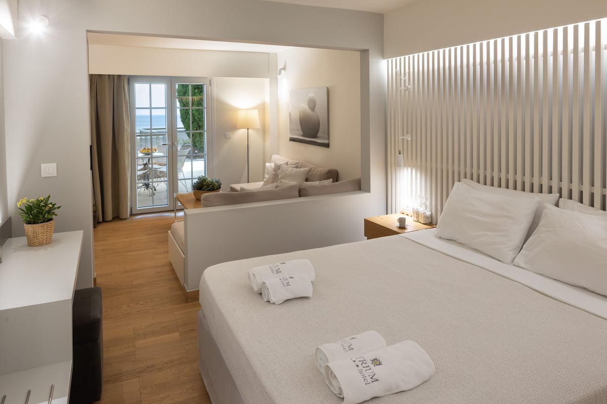 A modern hotel room with a large bed, a desk, and a balcony with a view.