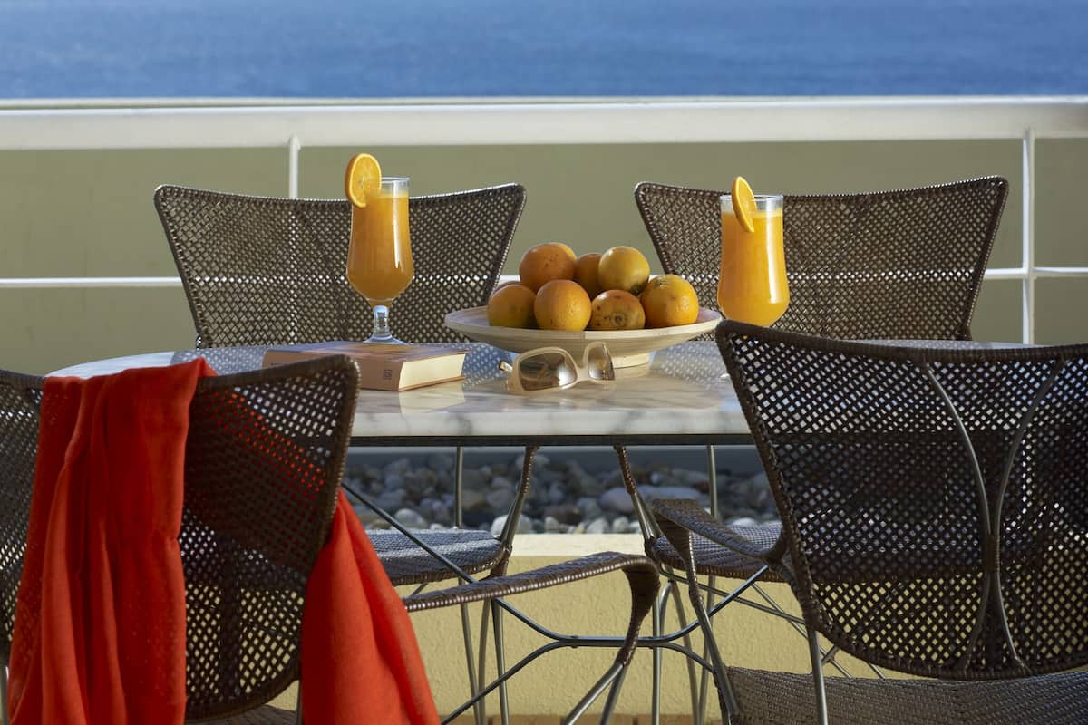 A table with a fruit bowl and drinks, overlooking the ocean.