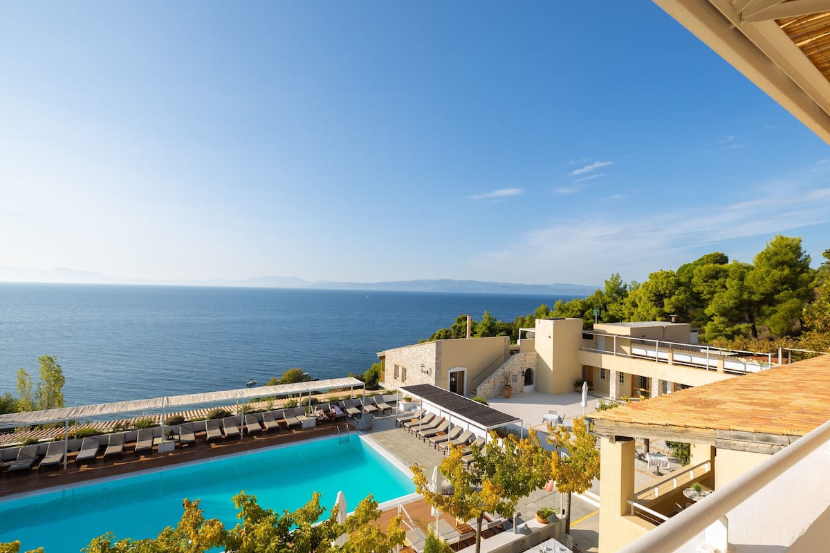 A pool area with a view of the sea, lounge chairs, and a building with a sloped roof.