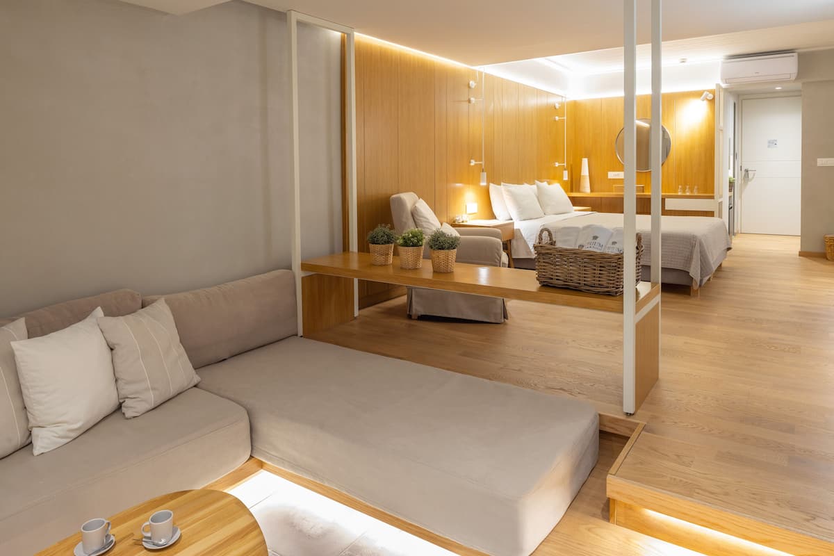 A modern hotel room with a sofa, a bed, a wooden table, and a small balcony area.