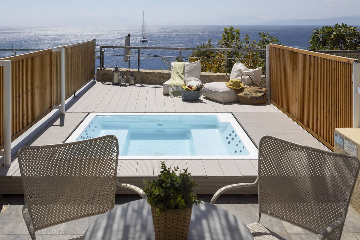 A rooftop terrace with a hot tub, wicker furniture, and a view of the ocean.