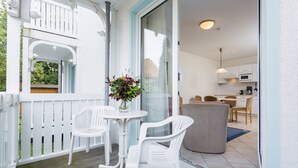 A balcony with white plastic chairs, a small round table, and a vase with flowers.