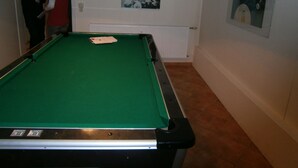 A pool table in a room with a radiator, a framed picture on the wall, and a door in the background.