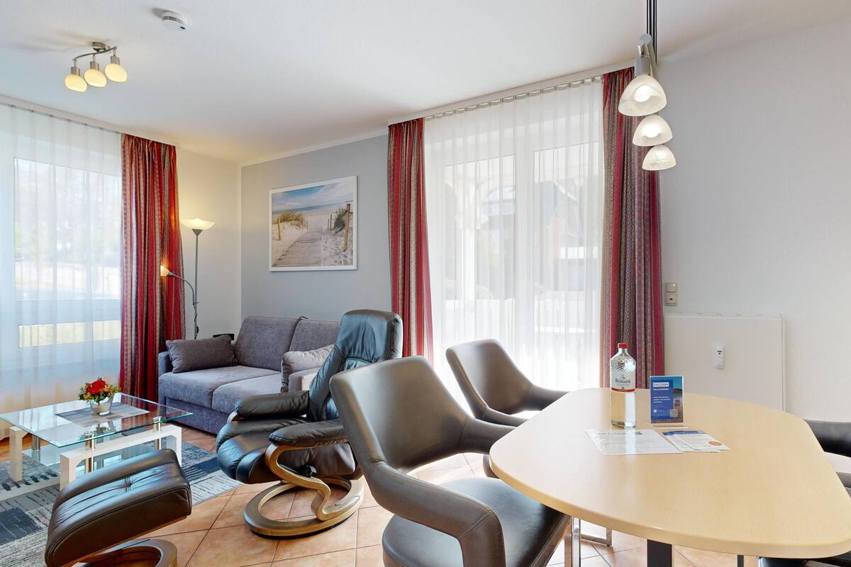 A modern hotel room with a sofa, two chairs, a glass coffee table, and a dining table.