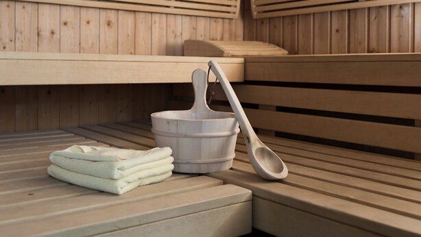 A sauna with wooden benches, a wooden bucket, and a folded towel.