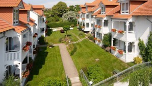 A row of white buildings with red-tiled roofs, a well-maintained lawn, and flower boxes on the balconies.