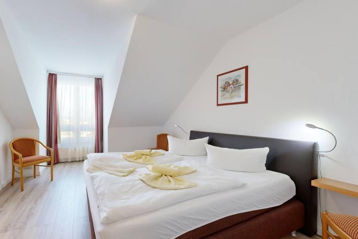 A hotel room with a bed, a chair, a desk, a lamp, and a window with curtains.
