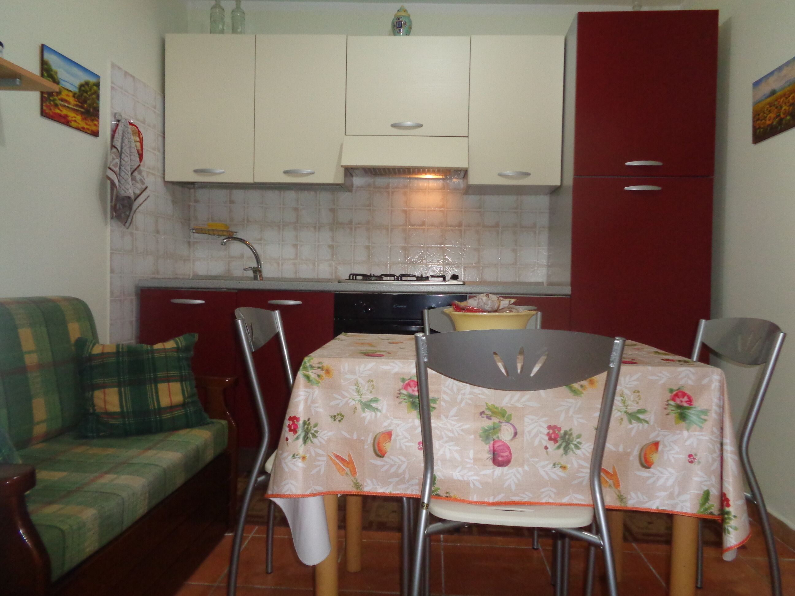 A compact kitchen with white cabinets, a red refrigerator, and a dining table with floral tablecloths.