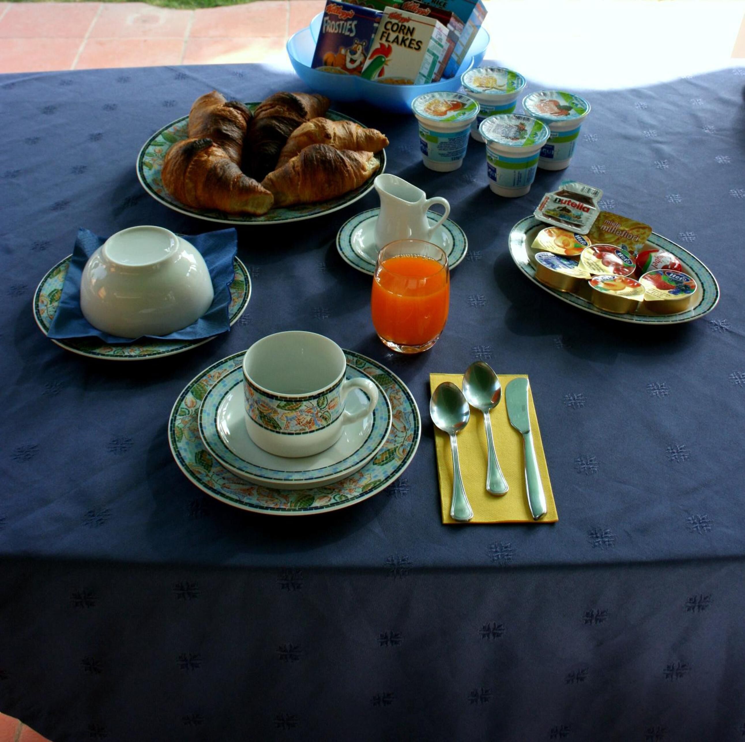 Una tavola imbandita per la colazione, con croissant, succo di frutta, yogurt e cereali.