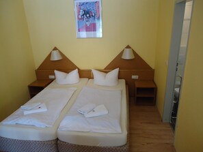 A hotel room with two single beds, each with a pillow and a folded towel. There are two bedside tables with lamps. A framed picture hangs on the wall above the beds. - Hotel Ottersleben (Magdeburg)