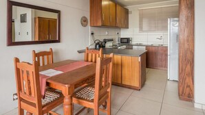 A compact kitchen with wooden cabinets, a dining table with chairs, a microwave, and a refrigerator.