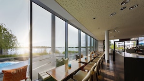 Een modern restaurant met grote ramen, houten tafels en stoelen, met uitzicht op een waterpartij.