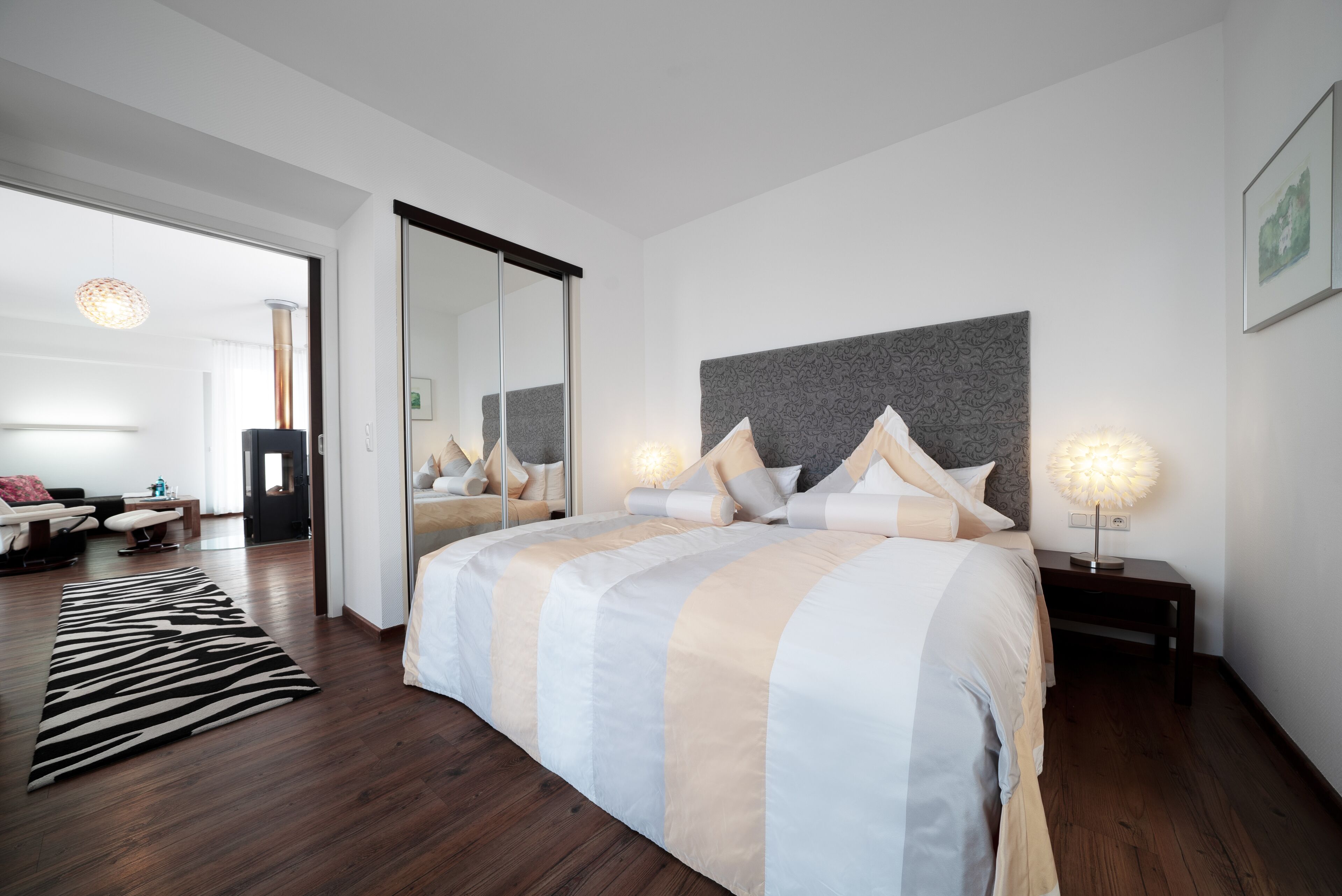 A modern bedroom with a large bed, a mirror, and a nightstand with a lamp.
