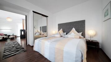 A modern bedroom with a large bed, a mirror, and a nightstand with a lamp.