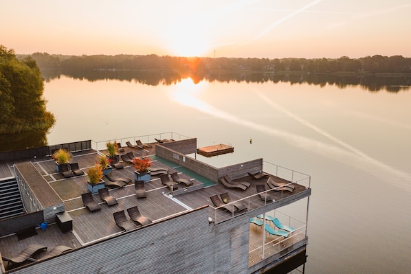 Een terras op het dak met meerdere zitgedeeltes, een zwembad en een uitzicht op een rustig meer bij zonsondergang.