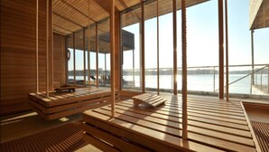 Een modern interieur met houten lamelvloeren, grote ramen en uitzicht op een waterpartij.