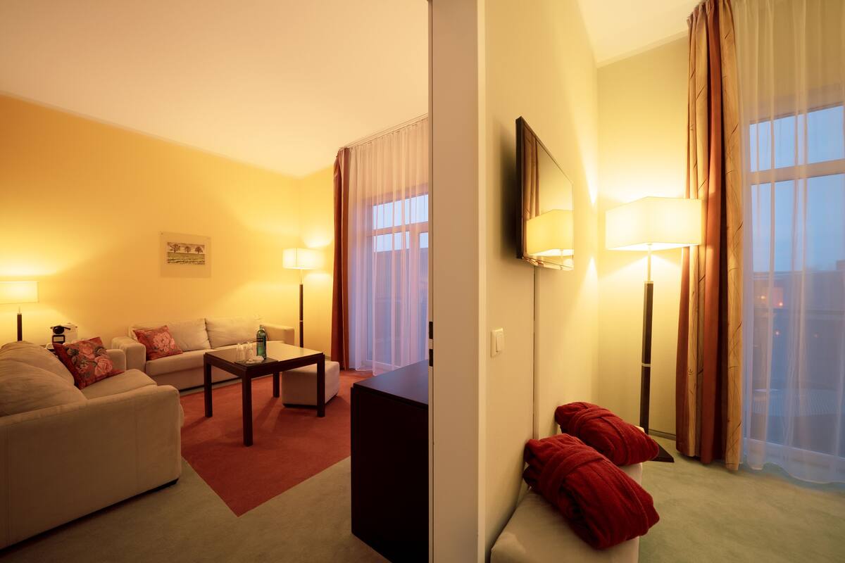Ein Hotelzimmer mit Wohnbereich, einer Couch, einem Couchtisch und einem an der Wand befestigten Fernseher.