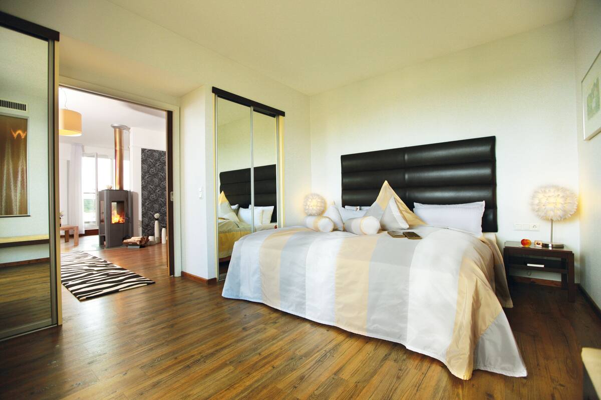 Ein modernes Schlafzimmer mit einem großen Bett, Holzboden, schwarzem Kopfteil und einem Spiegel.