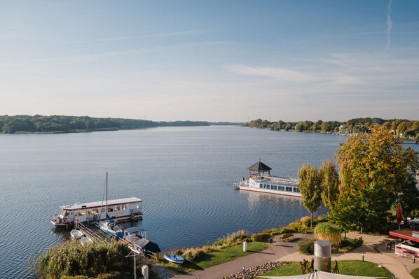 Une jetée au bord du lac, avec des bateaux, un kiosque et un espace vert aménagé avec des bancs et des arbres.