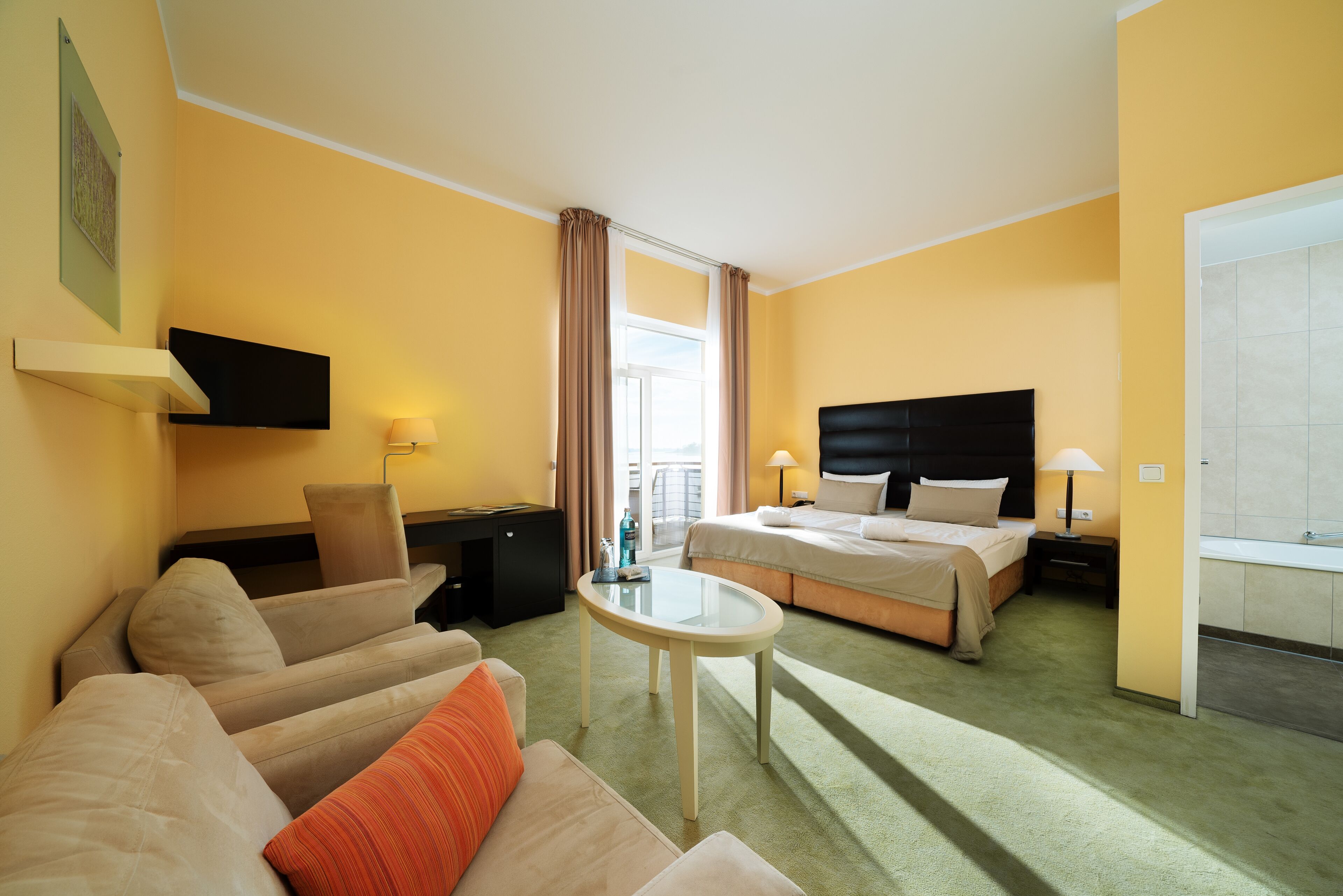 Een hotelkamer met een bed, een bank, een bureau, een televisie en een raam met gordijnen.