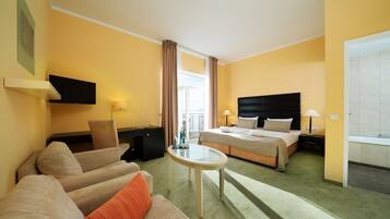 Een hotelkamer met een bed, een bank, een bureau, een televisie en een raam met gordijnen.