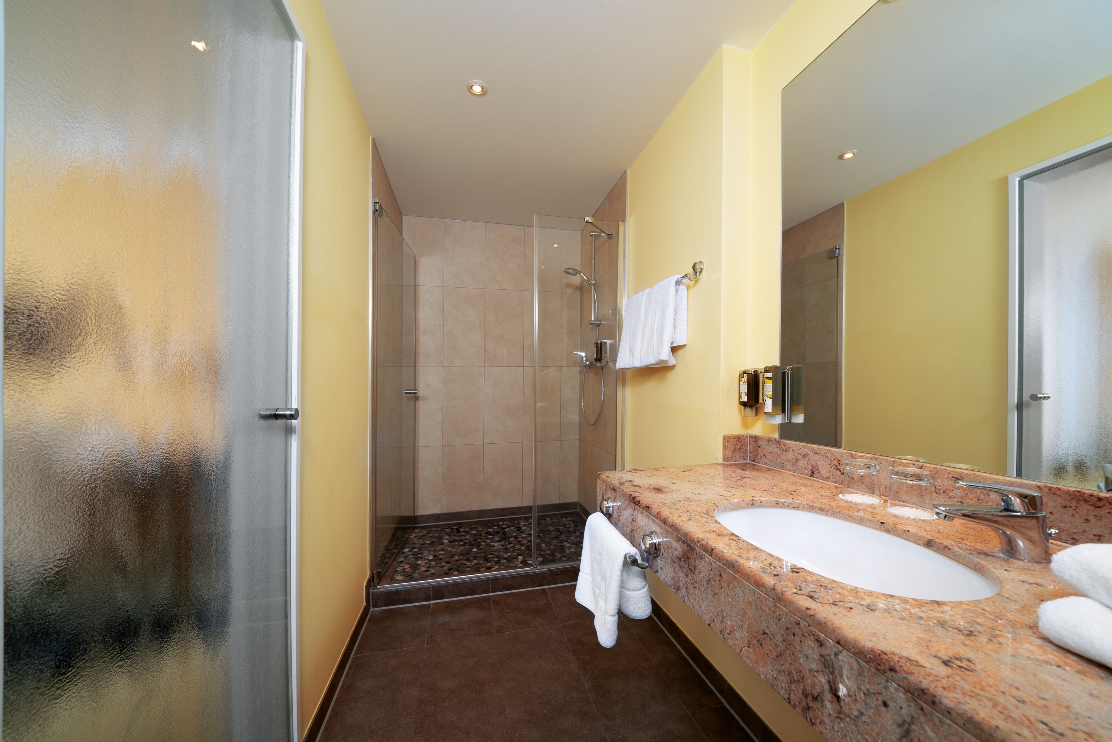 A bathroom with a glass shower enclosure, a marble sink, and a large mirror.