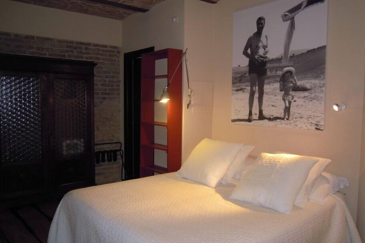 A bedroom with a bed, a wooden wardrobe, a red cabinet, and a wall-mounted picture.