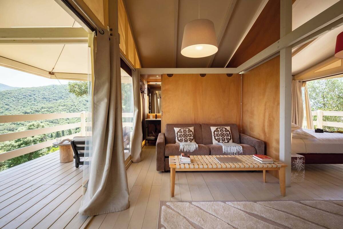 A cozy living area with a wooden sofa, a coffee table, and a view of a lush landscape.