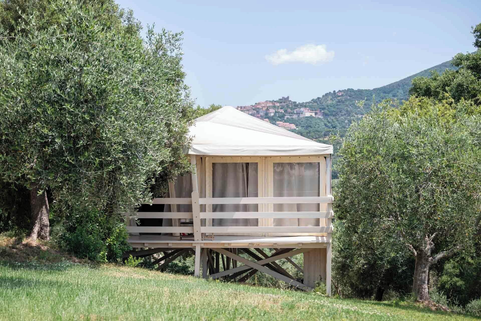 Une petite cabane en bois dotée d’un balcon, entourée d’arbres et se dressant sur un fond de collines.