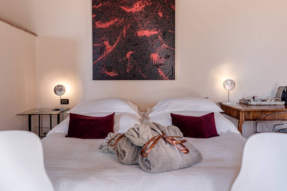 A hotel room with a bed, two bedside lamps, a desk with a lamp, and a large abstract painting on the wall.