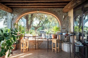 A rustic outdoor dining area with stone arches, wooden furniture, and potted plants.