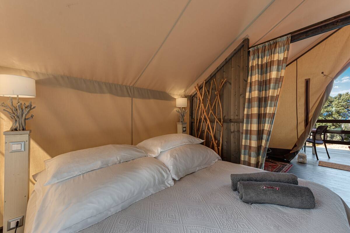 A tent-style room with a bed, pillows, a lamp, and a view of the outdoors.