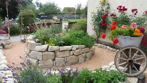 Een tuin met een stenen muur, een houten kar en diverse planten en bloemen.