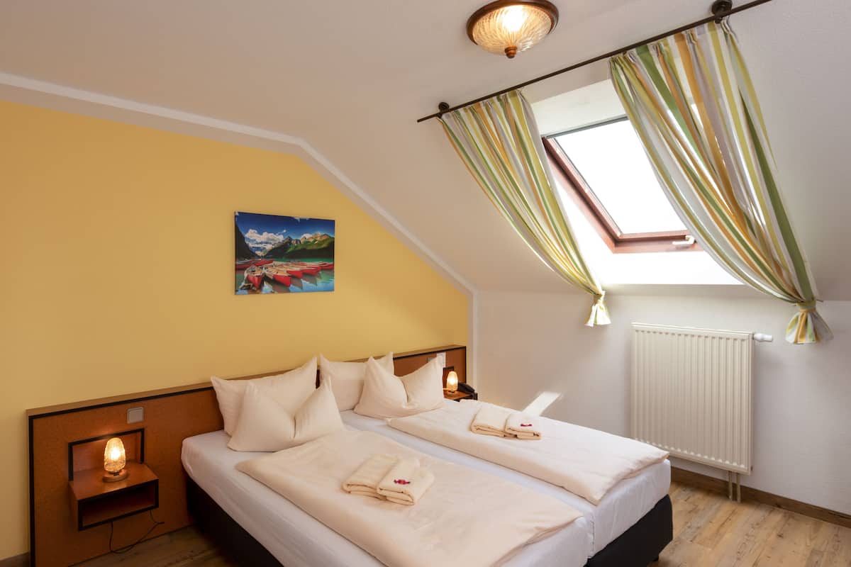 Une chambre avec deux lits, un tableau au mur, un puits de lumière et une fenêtre avec des rideaux.
