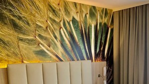 Een hotelkamer met een groot bed, twee kussens, een nachtkastje, een lamp en een muur met een patroon van pauwenveren.