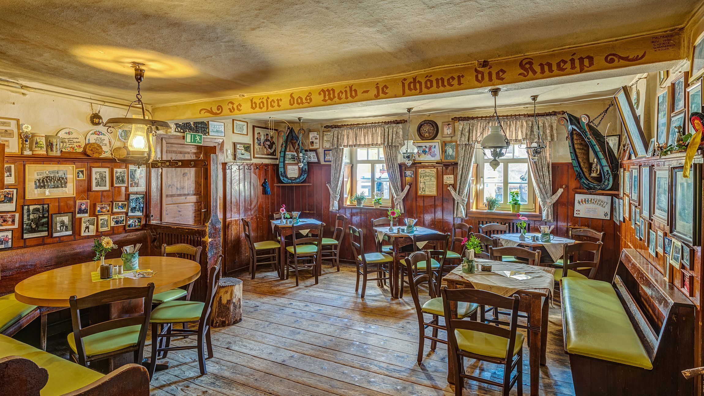 Eine traditionelle Kneipe mit Holzvertäfelung, mehreren Tischen und Stühlen sowie zahlreichen gerahmten Bildern und Erinnerungsstücken an den Wänden.