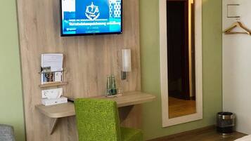 A hotel room with a bed, a desk with a chair, a TV mounted on the wall, and a mirror.