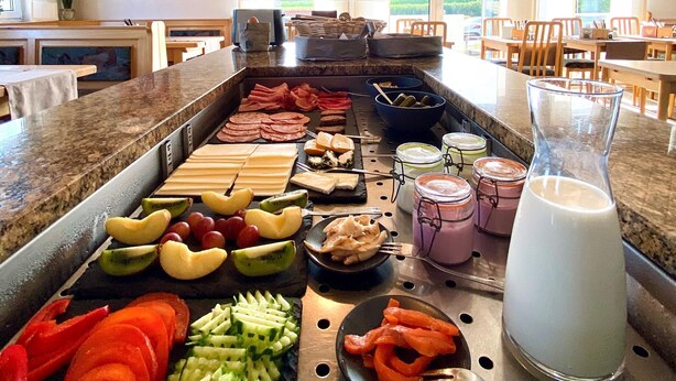 A buffet with various food items, a juice pitcher, and a view of the dining area. - Kleindienst (Ursensollen)