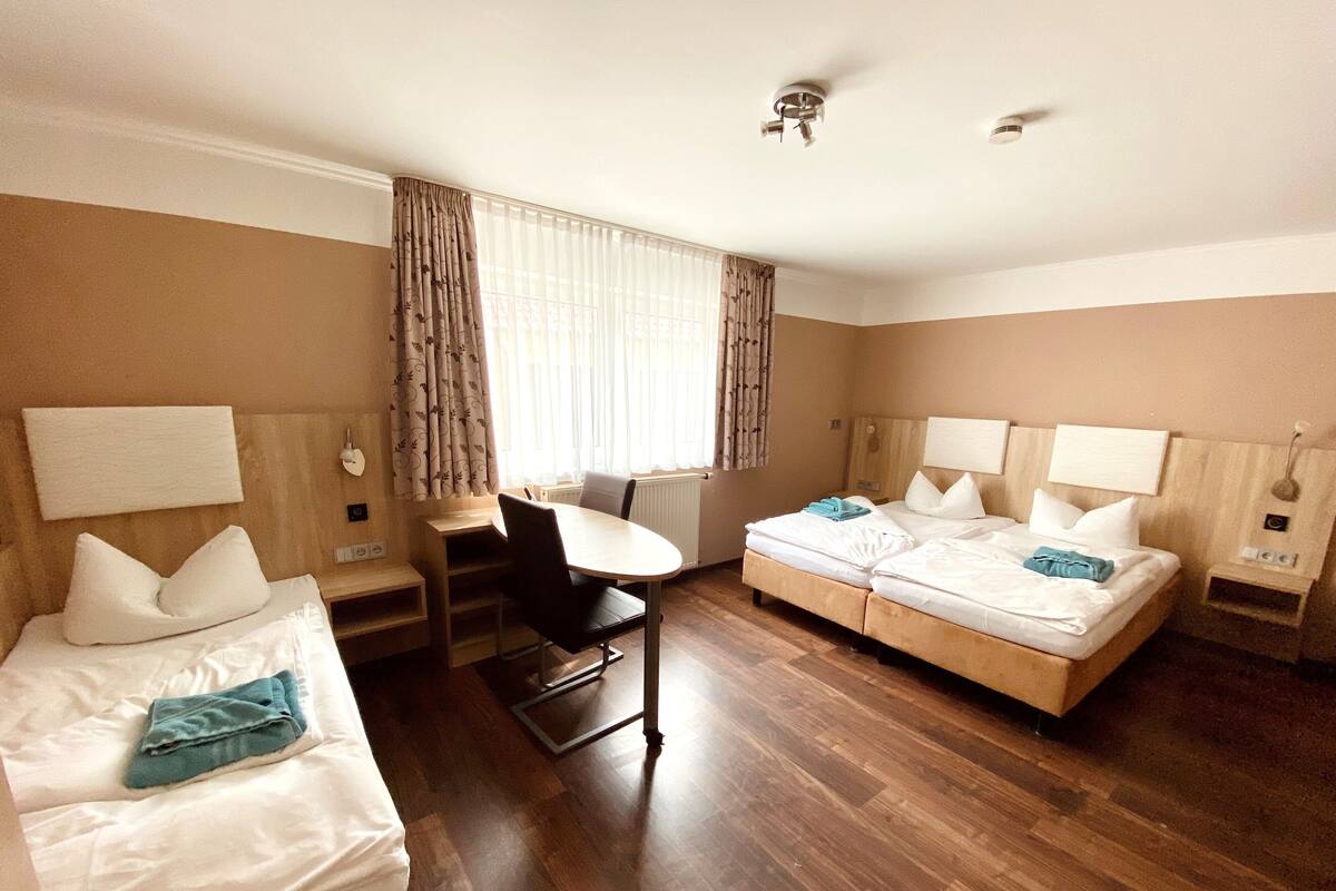 A hotel room with two single beds, a desk, and a chair.